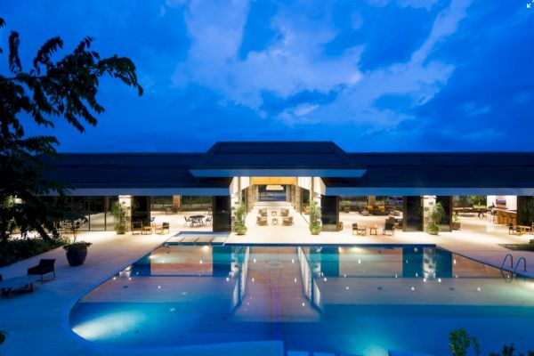 A luxurious modern building featuring an illuminated pool, surrounded by elegant outdoor seating, under a dramatic evening sky.