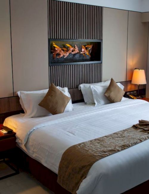 A neatly made hotel room with a large bed, two nightstands each with a lamp, and decorative pillows. Curtains cover a window.