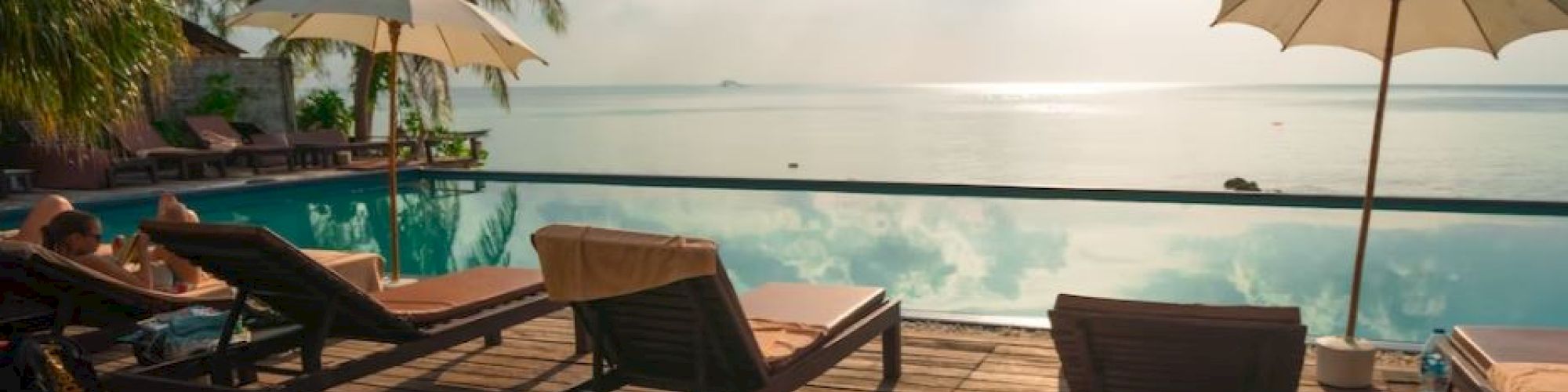 A serene poolside scene with lounge chairs, umbrellas, and a calm sea view under a partly cloudy sky.