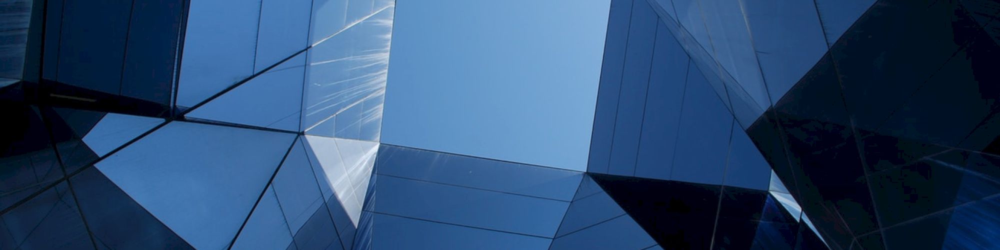 The image shows a geometric pattern of glass buildings reflecting light, creating a kaleidoscope effect with a clear sky visible in the center.