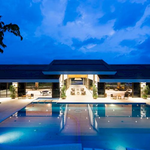 A luxurious building with a large, illuminated pool in the foreground is seen against a dusk sky.