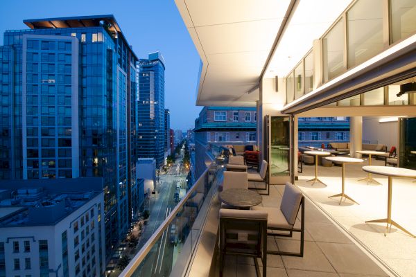 Rooftop terrace view at dusk showing a modern cityscape with tall buildings and a stylish, open-air seating area.