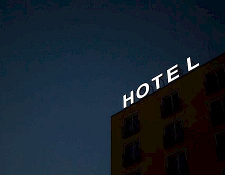 A building with a neon sign reads "HOTEL" against a dark sky, with one letter unlit.
