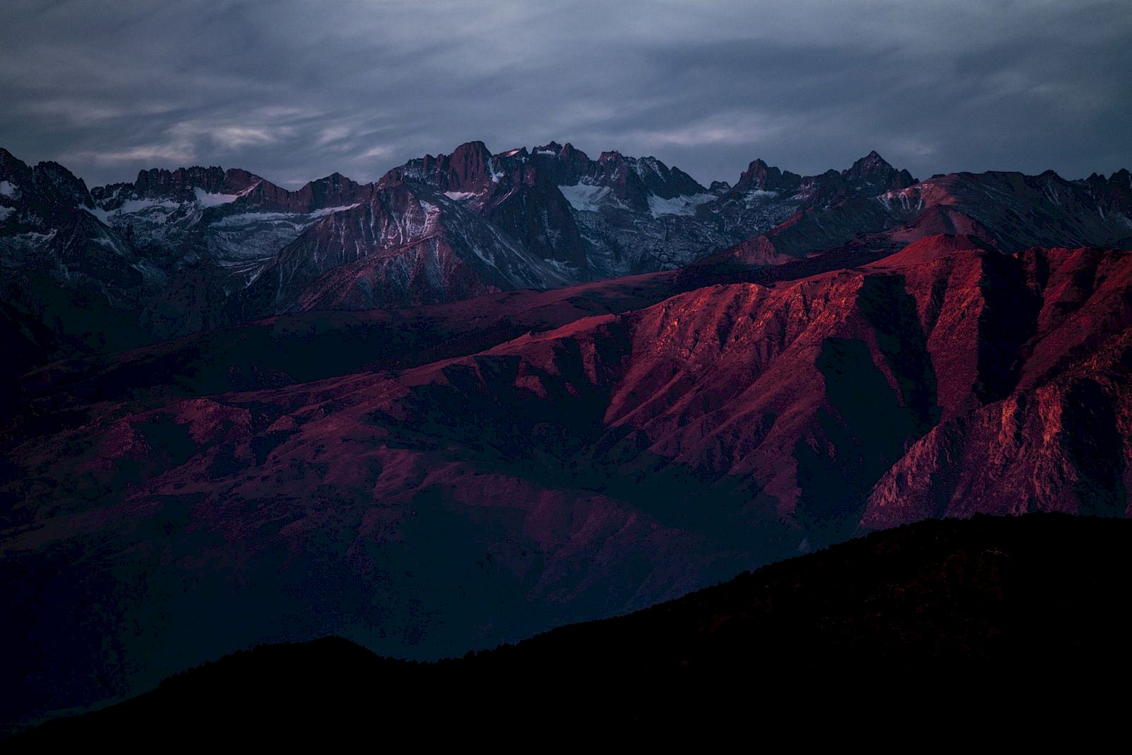 A dramatic mountain range with red and purple hues under a moody sky, creating a striking and atmospheric landscape.