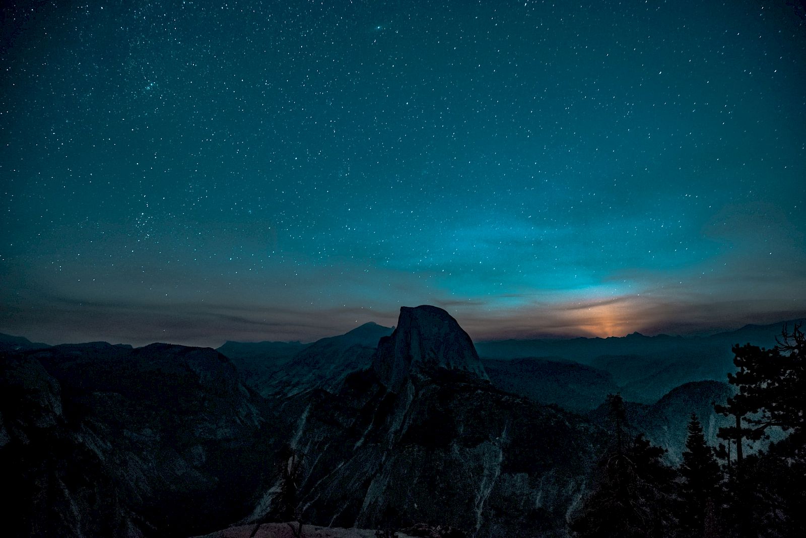 A mountainous landscape at night under a starry sky, with a glowing moonlight illuminating the horizon, creating a serene scene.