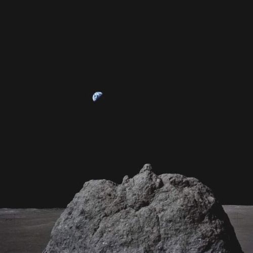 A rocky lunar surface with Earth visible in the distant dark sky, creating a striking celestial scene.