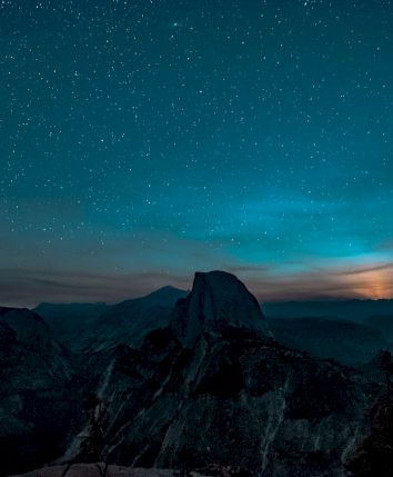 A night sky with stars, silhouetted mountains, and a glowing horizon, creating a serene and majestic landscape.