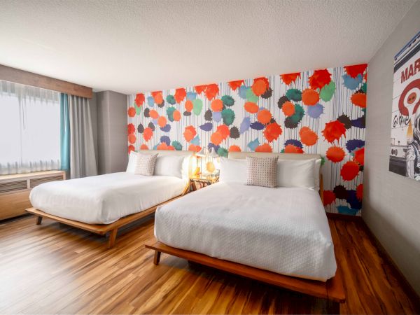 A hotel room with two beds, colorful floral wallpaper, a window with curtains, wooden floor, and a Mars-themed poster on the wall.