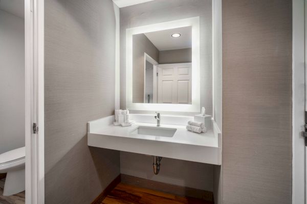 A modern bathroom vanity with an illuminated mirror, a sink, and neatly arranged towels is depicted in the image.