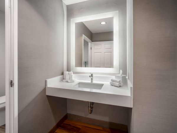 A modern bathroom vanity with an illuminated mirror, a sink, and neatly arranged towels is depicted in the image.