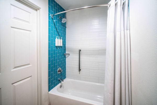 A modern bathroom features a bathtub with a shower, blue and white tiled walls, a curtain, and a grab bar.