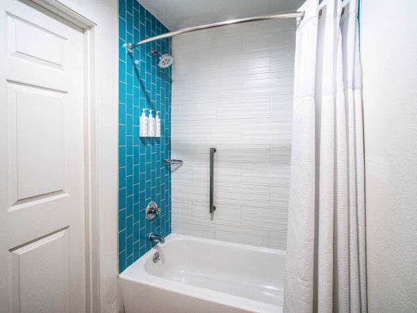 A modern bathroom features a bathtub with a shower, blue and white tiled walls, a curtain, and a grab bar.