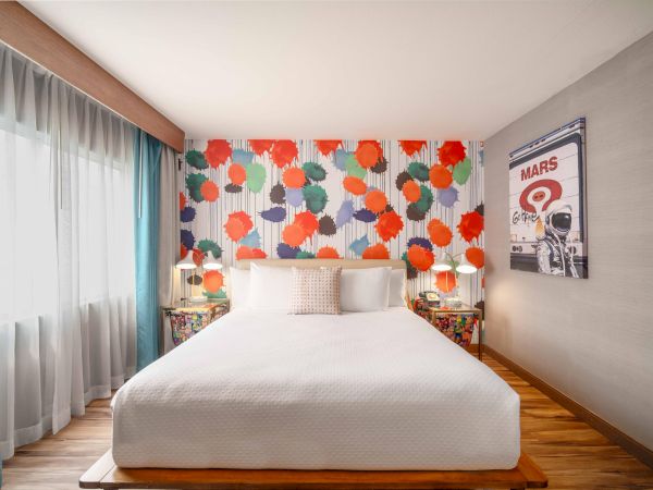 A brightly decorated bedroom with a colorful wall, large bed, two side tables, and a poster on the wall, well-lit by natural light.