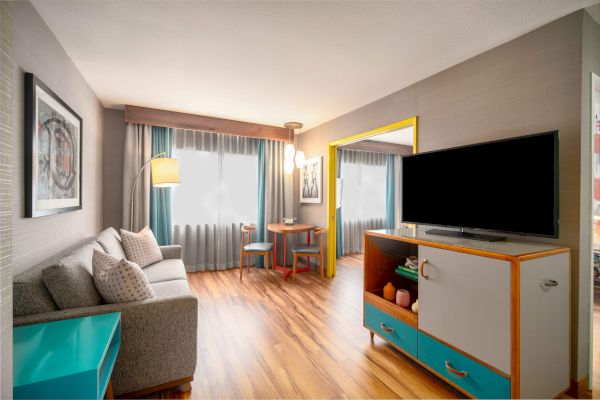A cozy living room with a sofa, a TV, and a small table, featuring wooden flooring and modern decor with blue and yellow accents.