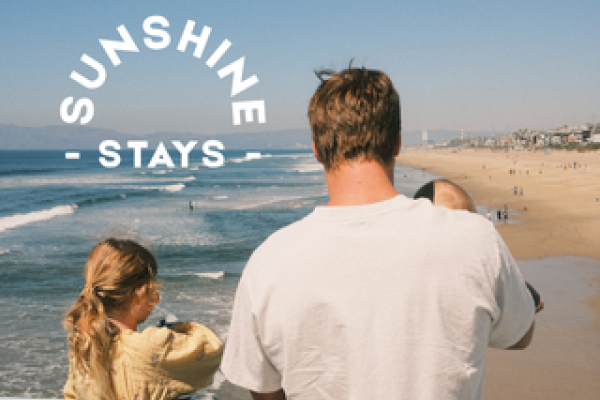 A person with children looks out over a sunny beach. Text reads "Sunshine Stays" in an arch above them.