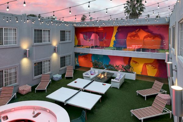 A stylish outdoor courtyard with seating, string lights, and vibrant mural walls, set under a colorful sky.