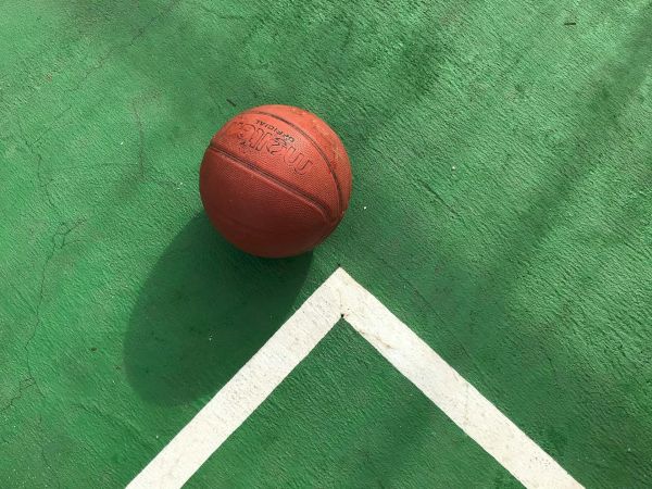A basketball on a green court surface, near white boundary lines, creating a simple yet dynamic scene.