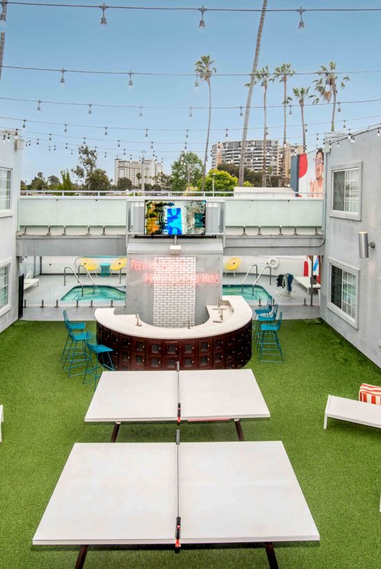 A courtyard with lounge chairs, a ping pong table, and a seating area under string lights, surrounded by white buildings.