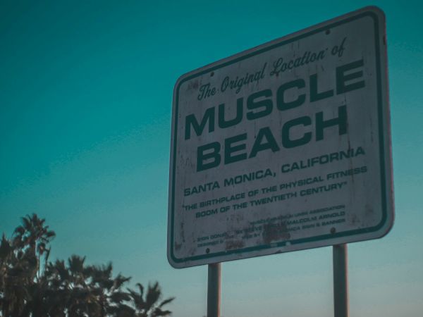 A sign for "Muscle Beach" in Santa Monica, California, highlighting its historical significance in fitness culture.