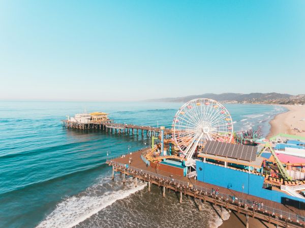 A seaside pier with a Ferris wheel, ocean waves, sandy beach, and clear blue sky creating a vibrant and sunny coastal scene.