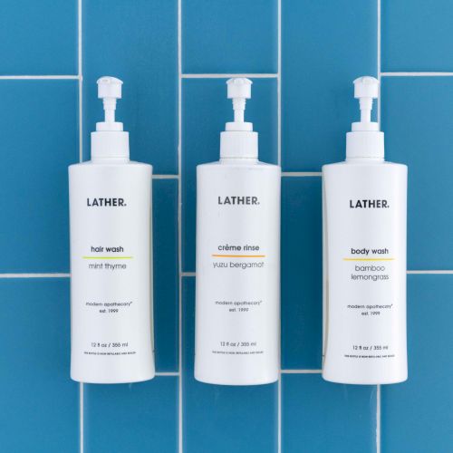 Three LATHER brand shower products with pumps against a blue tiled background.