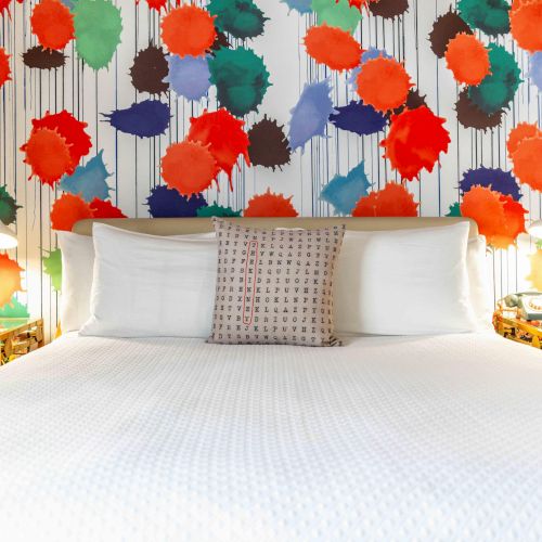 A bed with white linens, colorful wallpaper with leaf patterns in the background, flanked by side tables with lamps on each side of the bed.