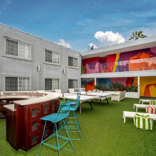 Outdoor patio with artificial grass, colorful wall mural, bar area, seating, and string lights in a courtyard setting.