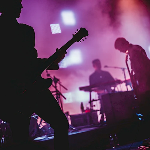 A silhouetted band performs on stage, with colorful lights creating a vibrant backdrop as they play their instruments.