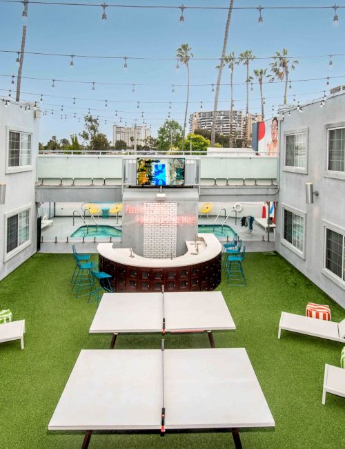 A courtyard with lounge chairs, a ping pong table, and a seating area under string lights, surrounded by white buildings.