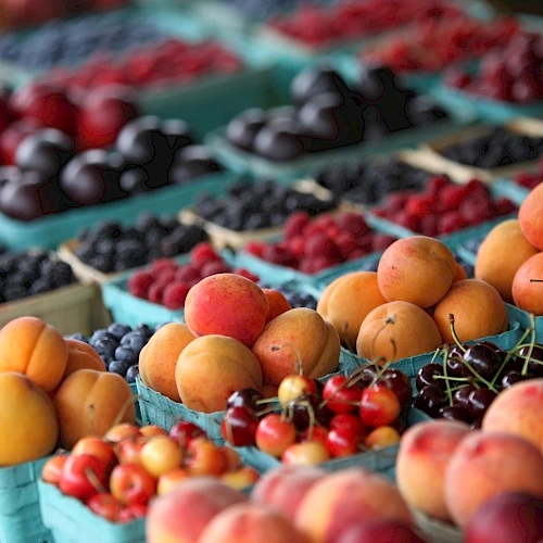 A colorful outdoor fruit market with peaches, apricots, berries, and berries arranged in crates.