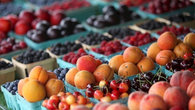 A colorful outdoor fruit market with peaches, apricots, berries, and berries arranged in crates.