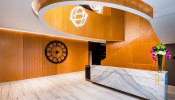A modern interior with a marble reception desk, wooden walls, a large clock, and decorative lighting fixtures.