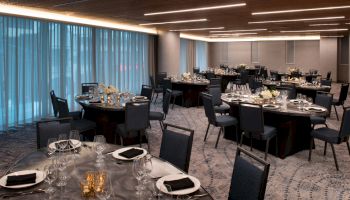 A banquet hall with round tables set up for an event, featuring elegant tableware and centerpieces, under ambient lighting.