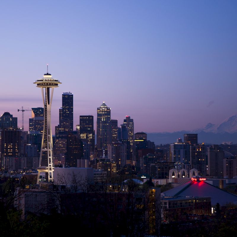 Seattle skyline at dusk, featuring the Space Needle and city buildings with Mount Rainier in the background.