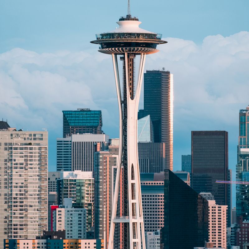 The image features the Space Needle with a backdrop of downtown skyscrapers under a blue sky with clouds.