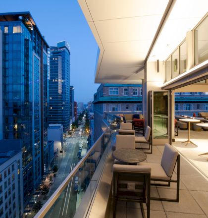A cityscape view from a balcony at dusk, featuring modern buildings and outdoor seating.