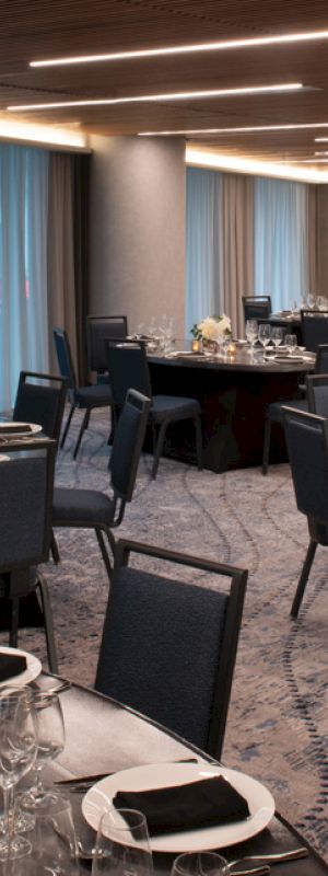 A banquet hall with round tables, set with black napkins, white flowers, and glassware, under a modern, lit ceiling.