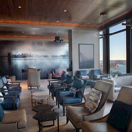 A modern lounge with comfortable seating, large windows offering a scenic view, and a mural on the wall, creating a relaxing atmosphere.