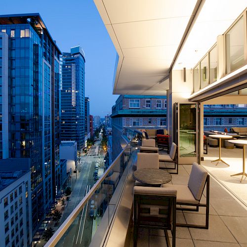 A modern rooftop terrace with seating overlooks an urban street lined with tall buildings, captured at dusk.