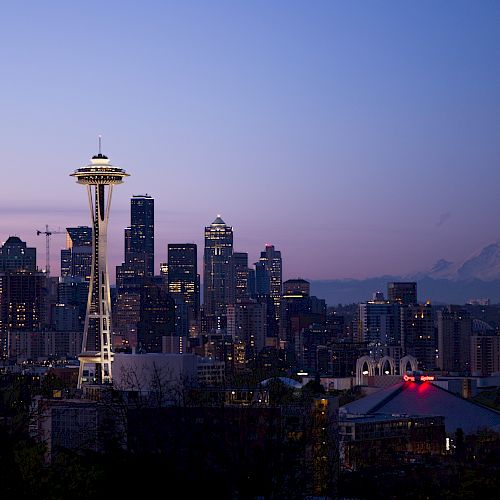 Seattle skyline at dusk with Space Needle, city buildings, and Mount Rainier in the background.