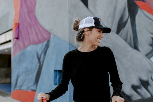 A person with a cap stands with a red bicycle, smiles at a colorful mural on a building wall in the background.