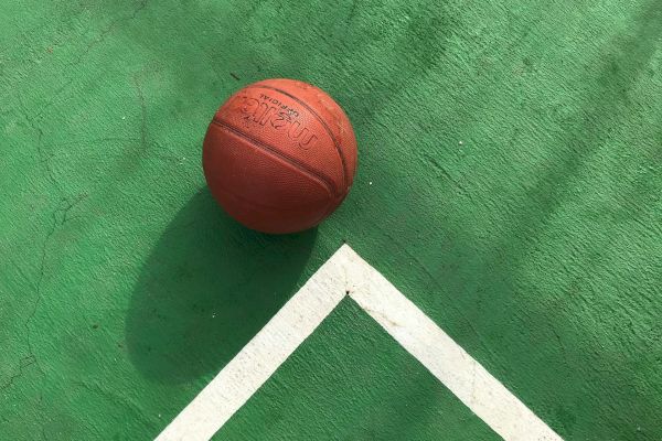 A basketball on a green court surface, near white boundary lines, creating a simple yet dynamic scene.