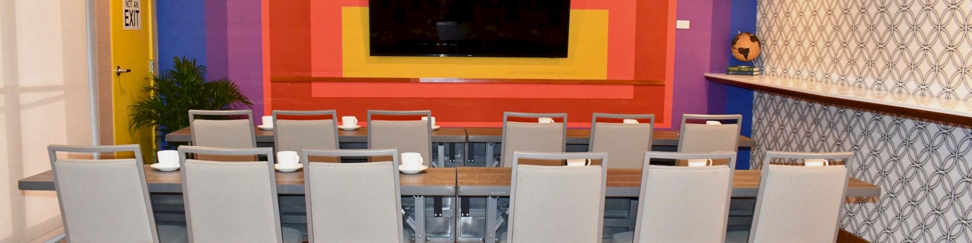 A conference room with a colorful wall, TV, and chairs arranged around a table.