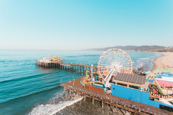 A seaside pier with a Ferris wheel, ocean waves, sandy beach, and clear blue sky creating a vibrant and sunny coastal scene.