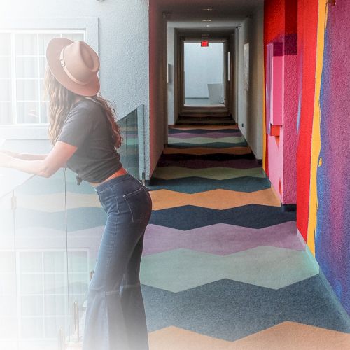 A person in a hat stands in a colorful hallway with geometric patterns on the floor and vibrant wall art.