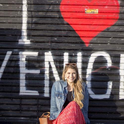 A person is sitting in front of a mural that says "I ♥ Venice." The mural features large white letters on a black background with a red heart.