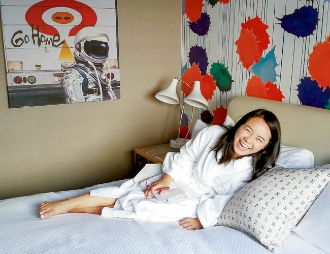 A person in a white robe on a bed, with colorful wall art and a Mars-themed poster in the background.
