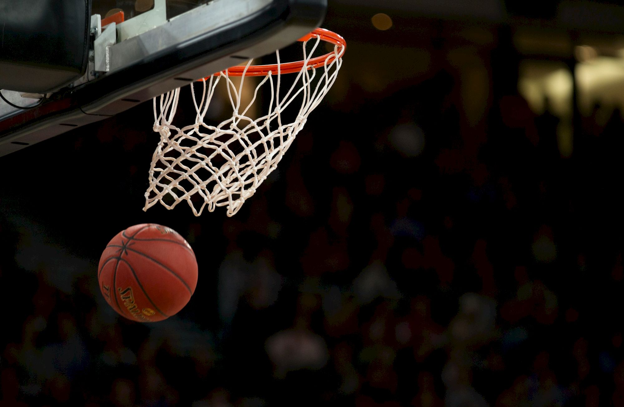 A basketball about to go through a hoop, with a net visible, set against a dark background.
